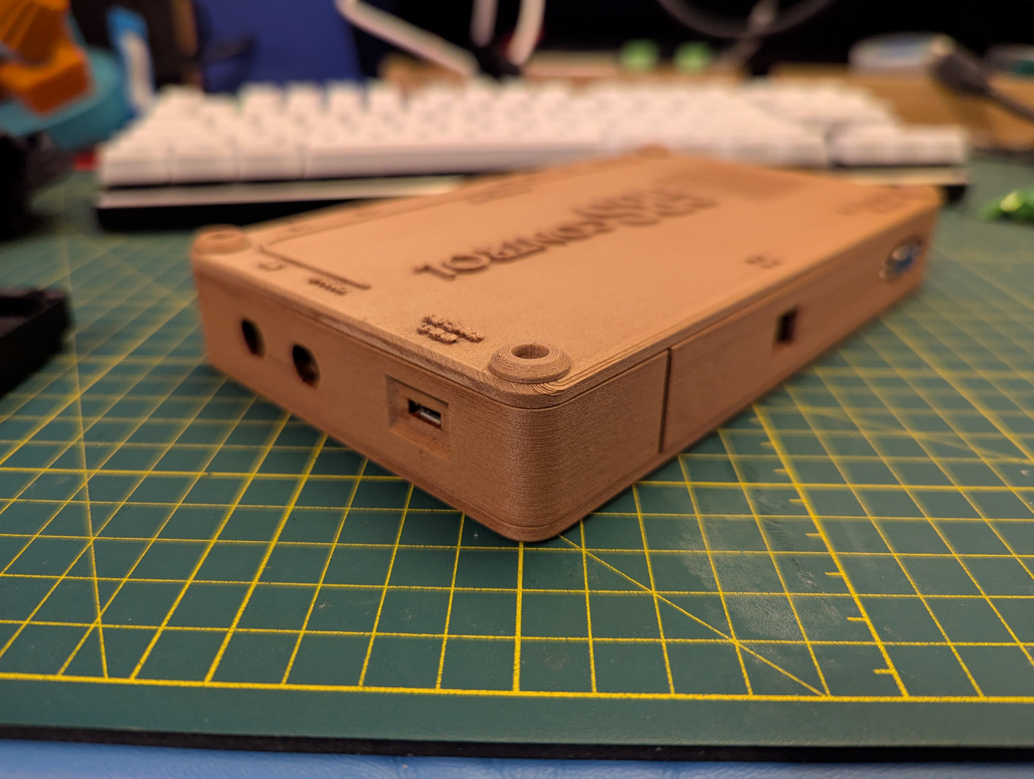A photograph of a GBS-Control upscaler device.  The electronics are installed in a 3D-printed box that has been colored with wood stain, giving it a 'faux wood grain' appearance, with legends for the inputs and outputs printed standing out from the surface of the top of the box.